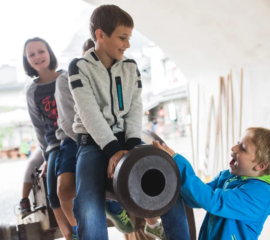 Lachende Kinder spielen auf einer alten Kanone in einem historischen Freilichtmuseum